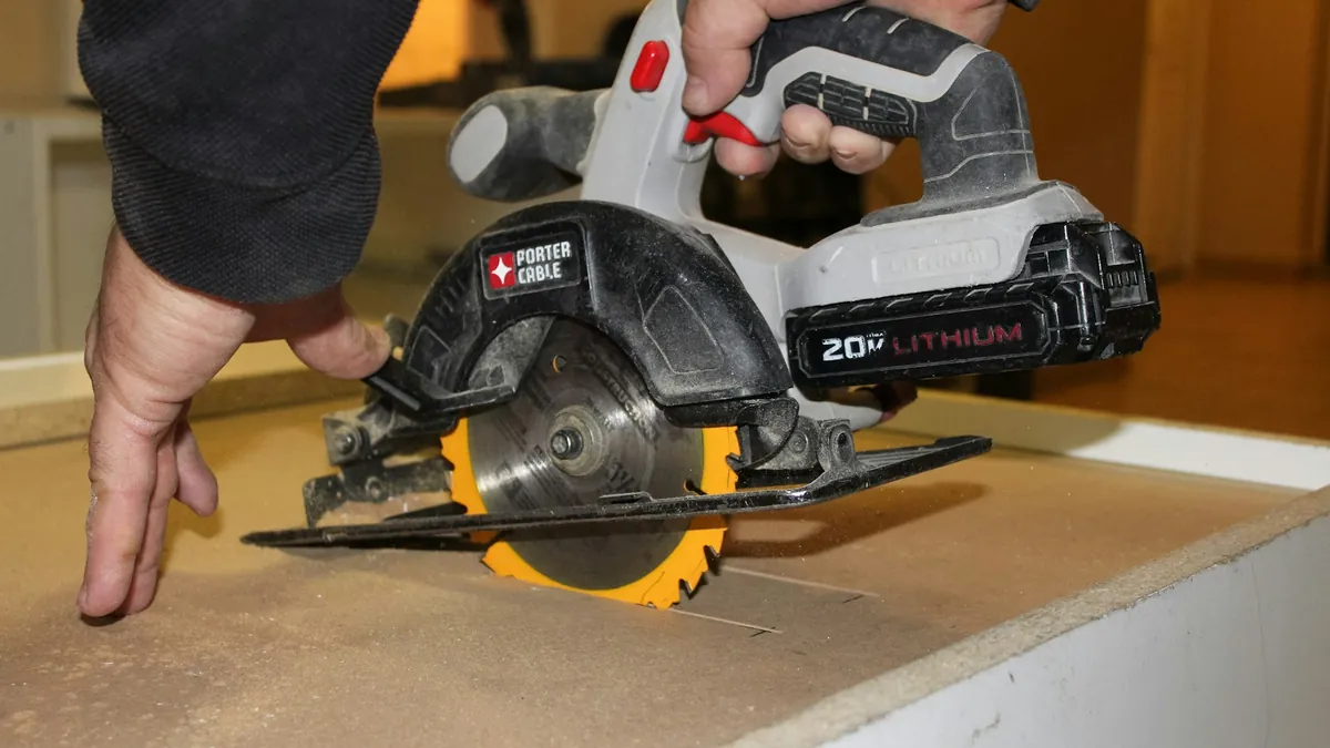 Hands operating a cordless circular saw on a wood panel.