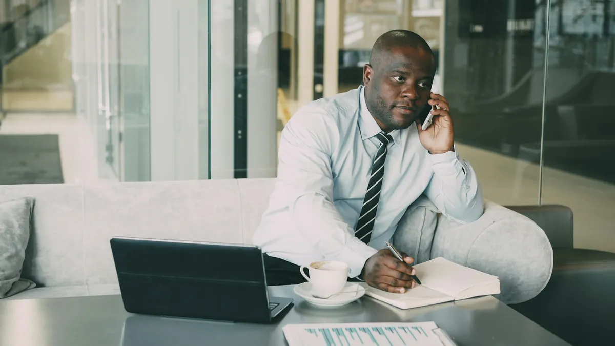 Man taking notes in a notebook while speaking on a phone.
