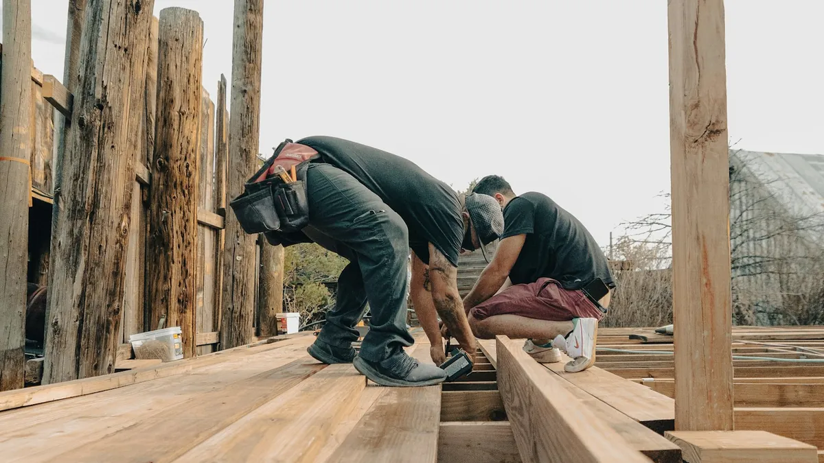 Two contractors framing a wooden deck at a residential construction site